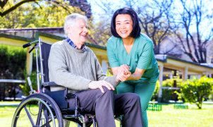 senior man on wheelchair with female medical staff smiling